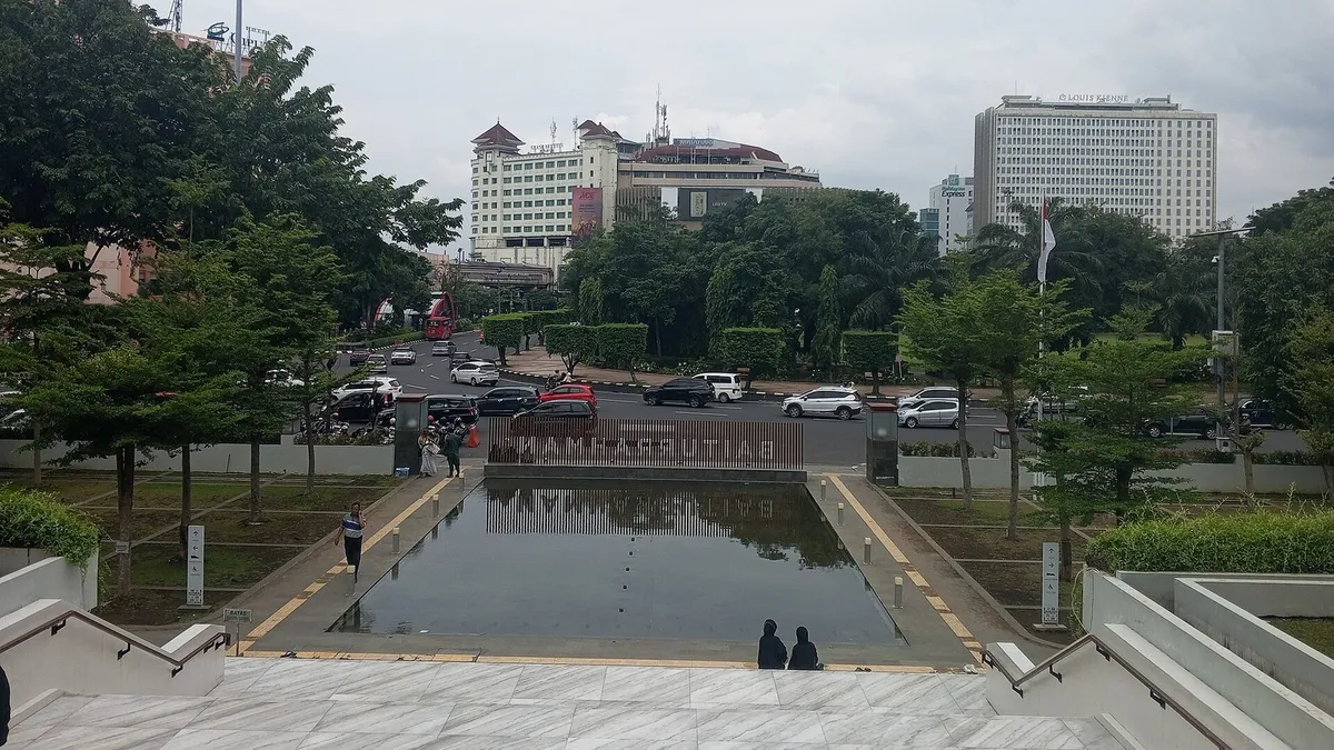 Kawasan Simpang Lima Semarang dilihat dari pelataran masjid: kolam dan tangga di latar depan, jalan raya dengan mobil dan pepohonan, serta beberapa gedung bertingkat di latar belakang