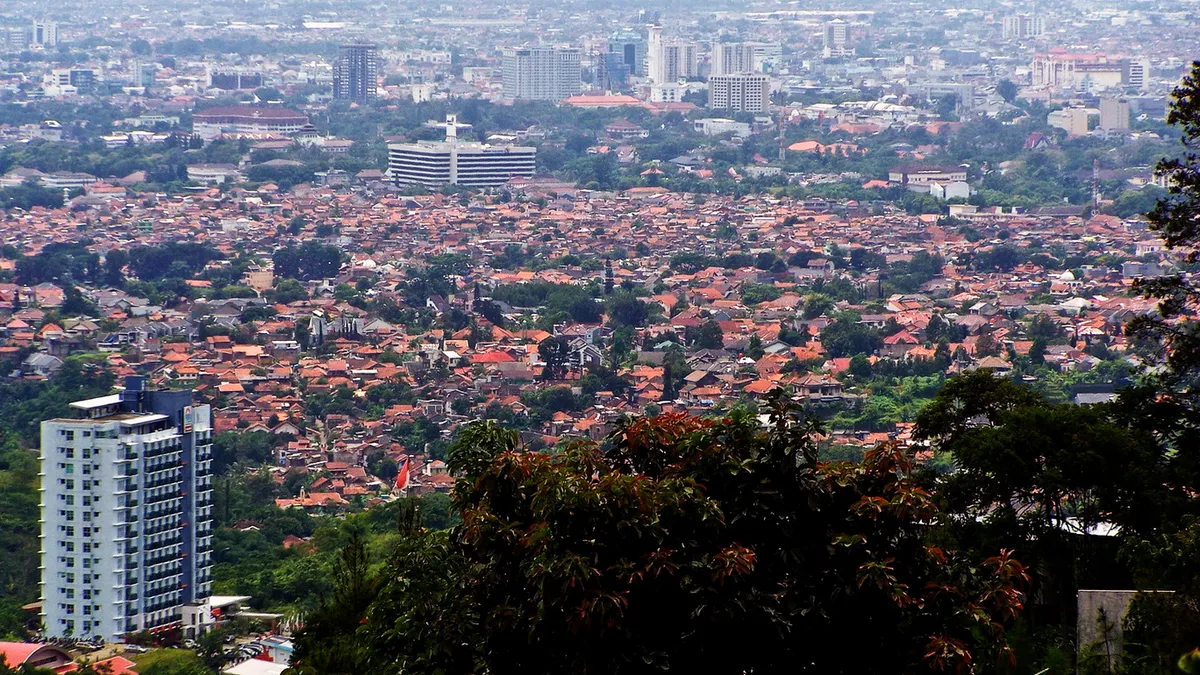 Sebagian Kota Bandung dilihat dari dataran tinggi Dago pada Januari 2011: hamparan permukiman padat beratap genteng merah, gedung bertingkat di kejauhan, dan satu gedung tinggi di sisi kiri